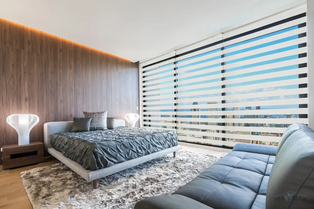 White dual shades on large bedroom windows with a city skyline view.