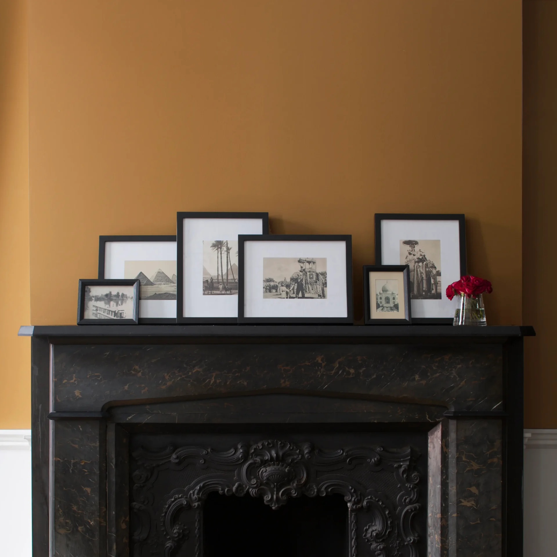 Framed black-and-white photos displayed on a dark marble fireplace mantel set against an ochre-yellow accent wall.
